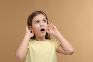 Photo of Little girl with hearing problem on pale brown background