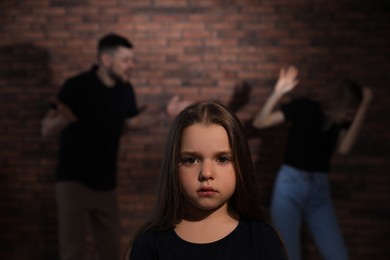 Photo of Couple fighting indoors, focus on their unhappy little daughter. Domestic violence