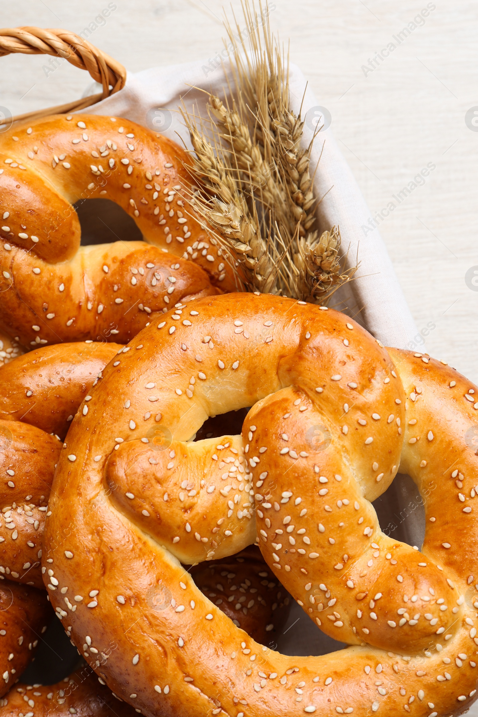 Photo of Basket with delicious pretzels and wheat spikes on white table, closeup
