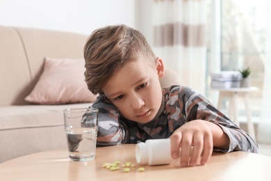 Photo of Little child with pills and water at table indoors. Danger of medicament intoxication