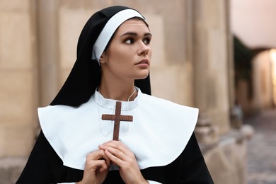 Young nun with Christian cross near building outdoors