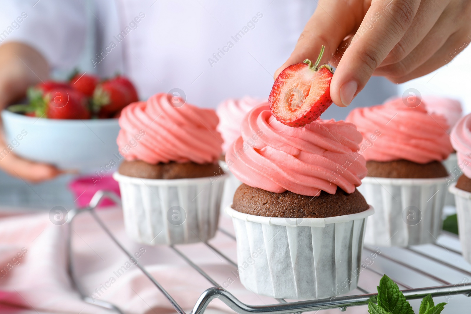Photo of Woman decorating delicious cupcakes with fresh strawberries at table, closeup