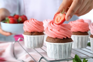 Woman decorating delicious cupcakes with fresh strawberries at table, closeup