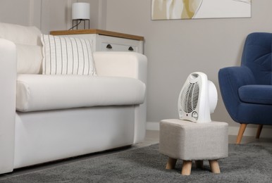 Photo of Electric fan heater on pouf in living room