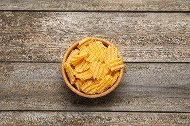 Bowl with delicious ridged potato chips on wooden table, top view