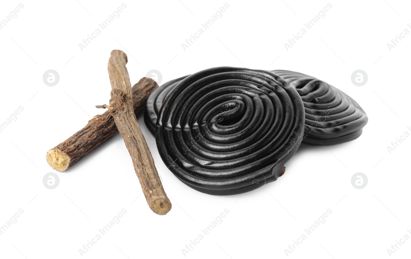 Photo of Tasty black candies and dried sticks of liquorice root on white background