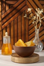 Photo of Natural honeycombs and honey in bowl on white table, space for text