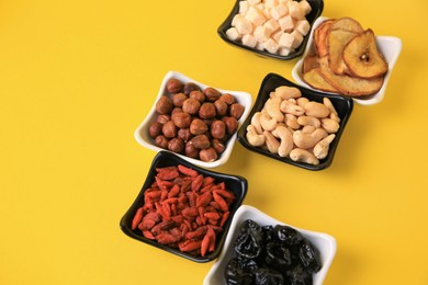 Photo of Bowls with dried fruits and nuts on yellow background. Space for text