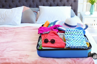 Photo of Open suitcase with beach clothes and accessories on bed indoors