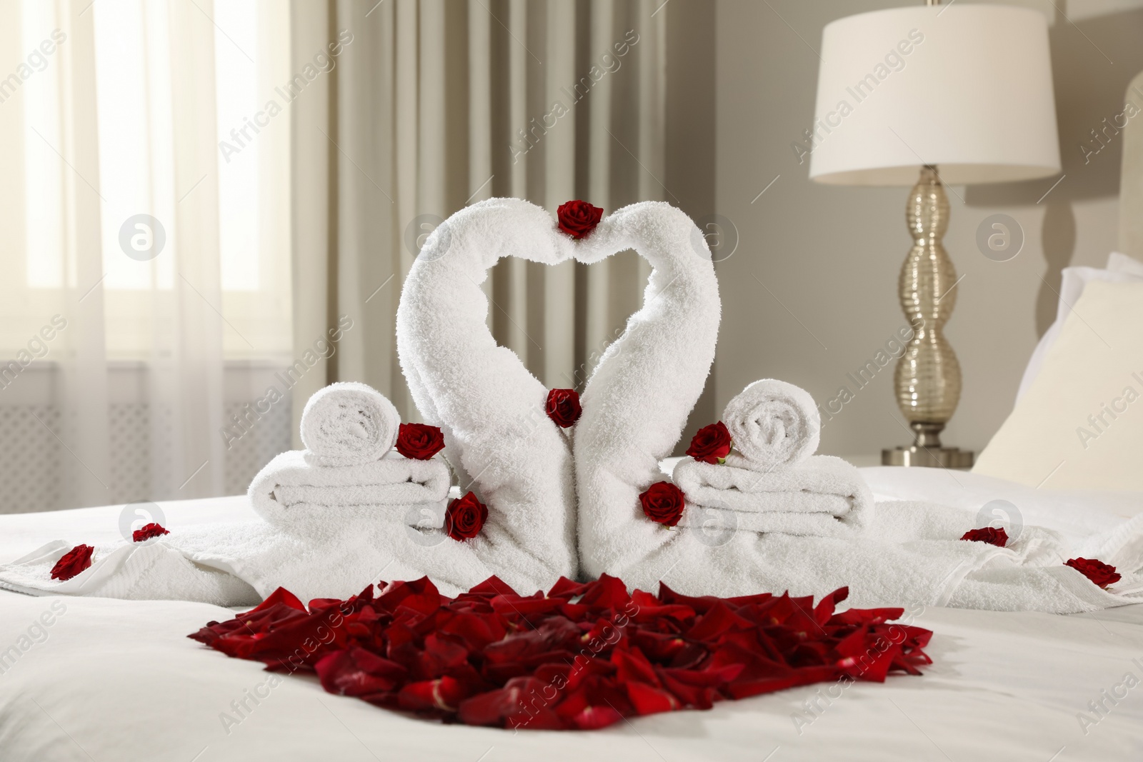 Photo of Beautiful swans made of towels and red rose petals on bed in room