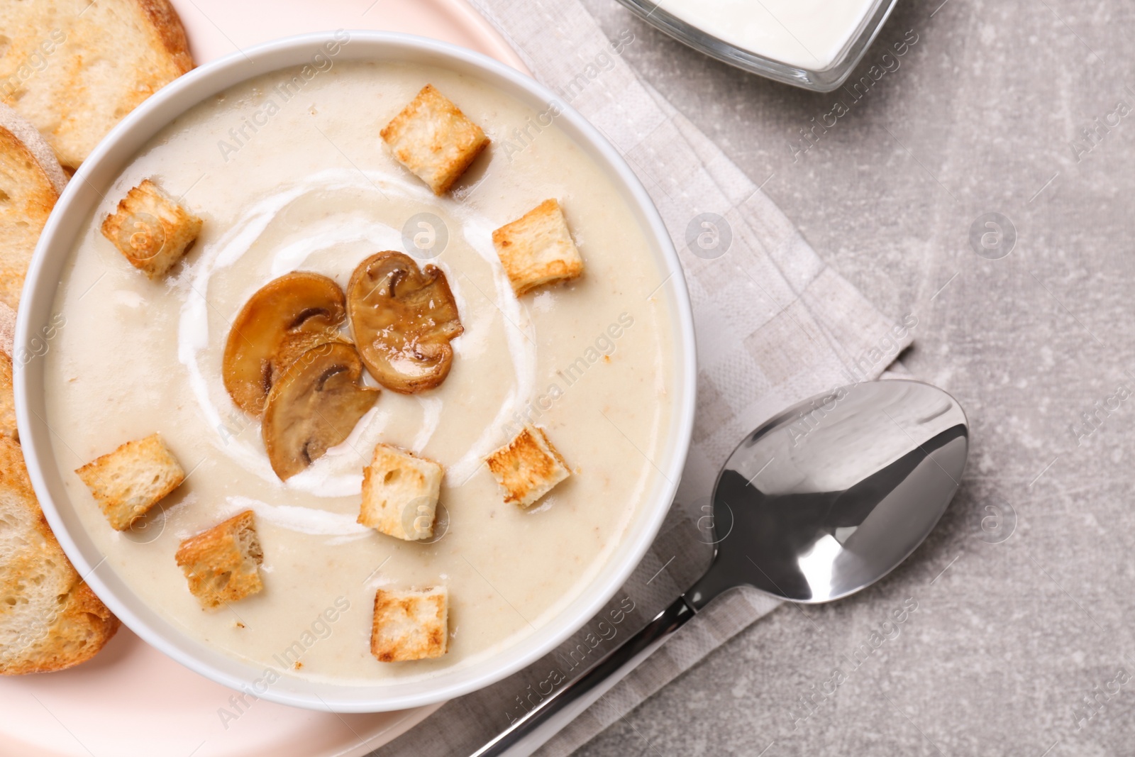 Photo of Delicious cream soup with mushrooms and croutons served on grey table, flat lay