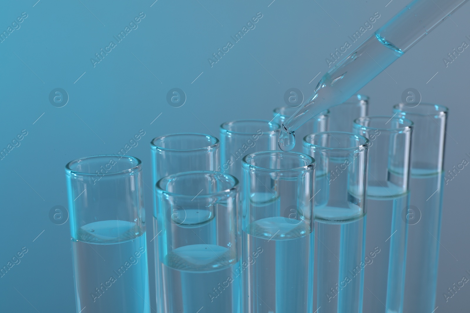 Photo of Laboratory analysis. Dripping liquid from pipette into glass test tube on light blue background, closeup