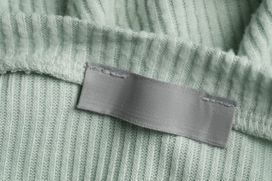 Photo of Empty clothing label on light green garment, top view