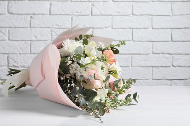 Photo of Bouquet of beautiful flowers on wooden table against white brick wall. Space for text