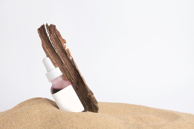 Photo of Bottle with serum and bark on sand against white background, space for text. Cosmetic product