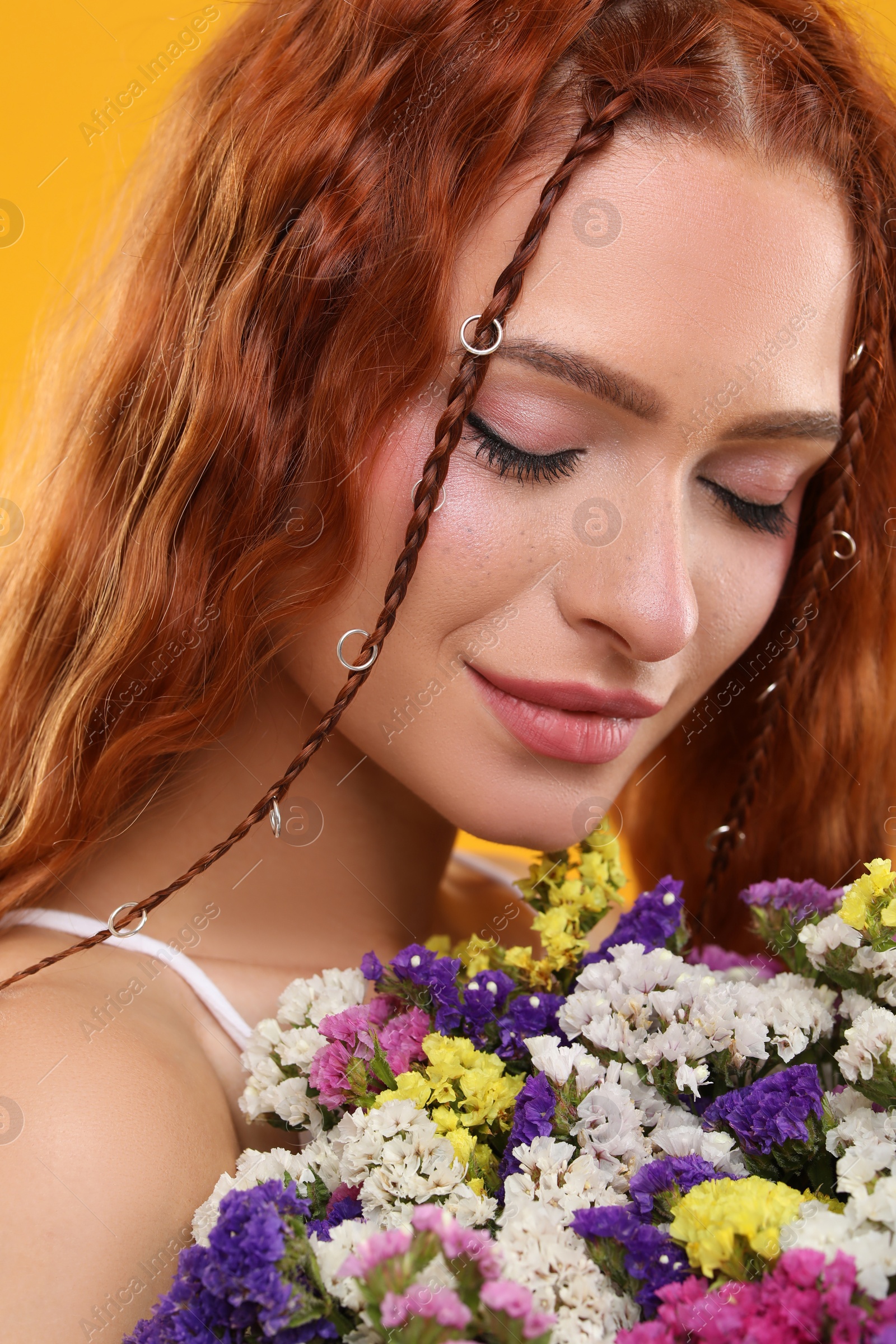 Photo of Beautiful young hippie woman with bouquet of colorful flowers on orange background, closeup