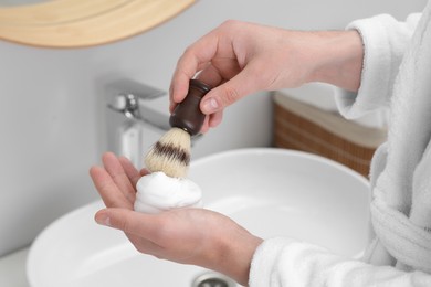 Photo of Man applying shaving foam onto brush in bathroom, closeup