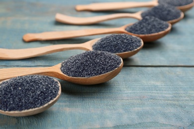 Poppy seeds in spoons on blue wooden table, closeup