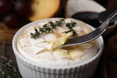 Photo of Eating tasty baked camembert with fork from bowl at table, closeup