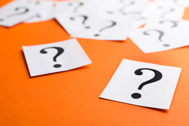 Photo of Paper notes with question marks on orange background, closeup