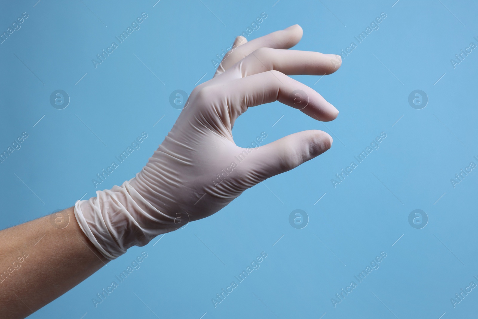 Photo of Doctor wearing white medical glove holding something on light blue background, closeup