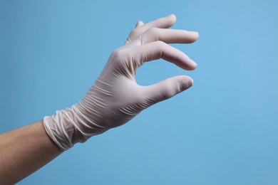 Doctor wearing white medical glove holding something on light blue background, closeup