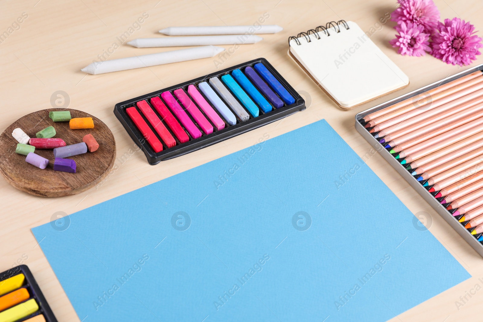 Photo of Blank paper, soft pastels and drawing pencils on wooden table at artist's workplace. Space for design