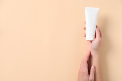 Woman with tube of hand cream on beige background, top view. Space for text