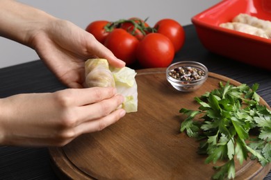 Woman preparing stuffed cabbage roll at table, closeup