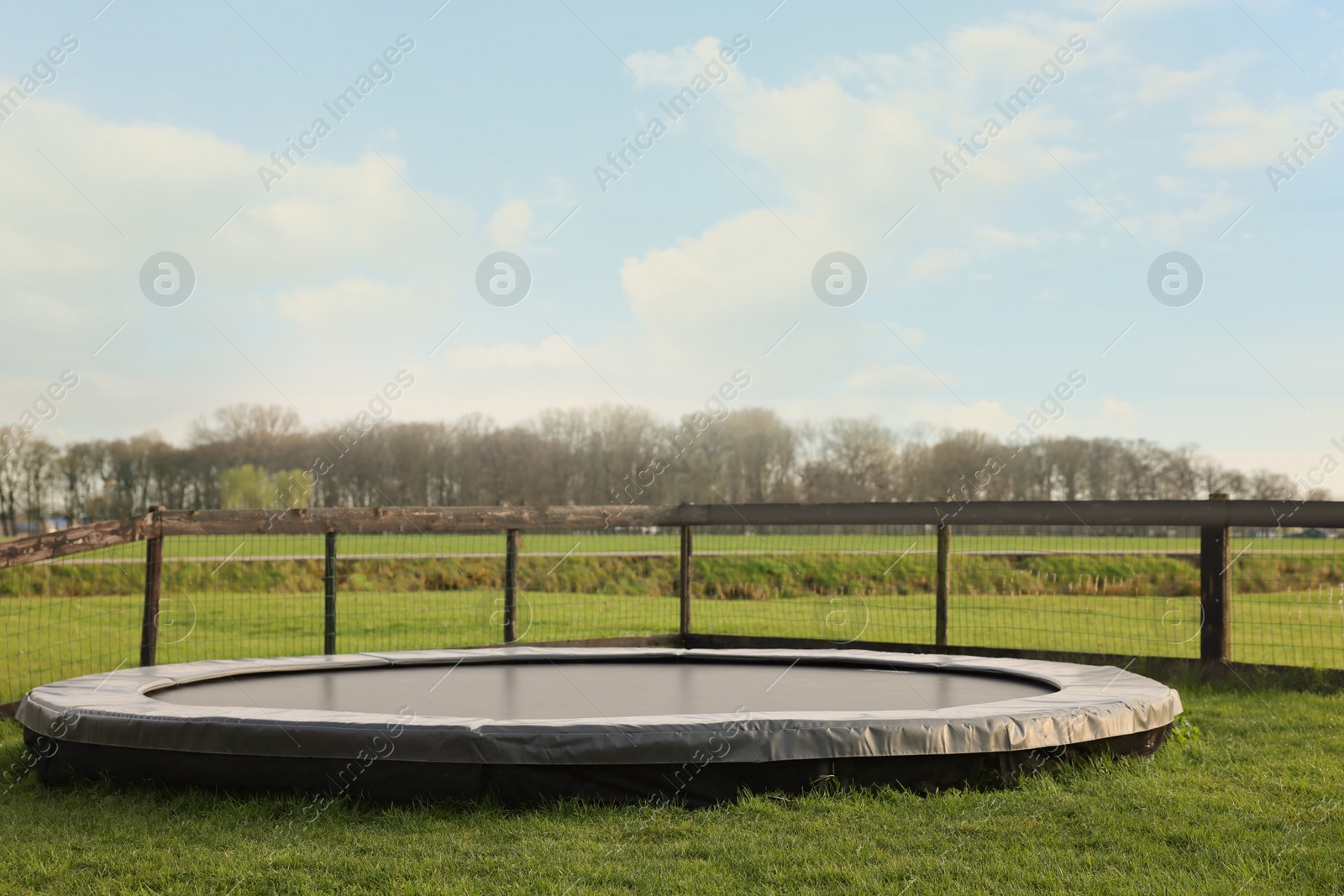 Photo of Big trampoline near wooden fence on green lawn outdoors