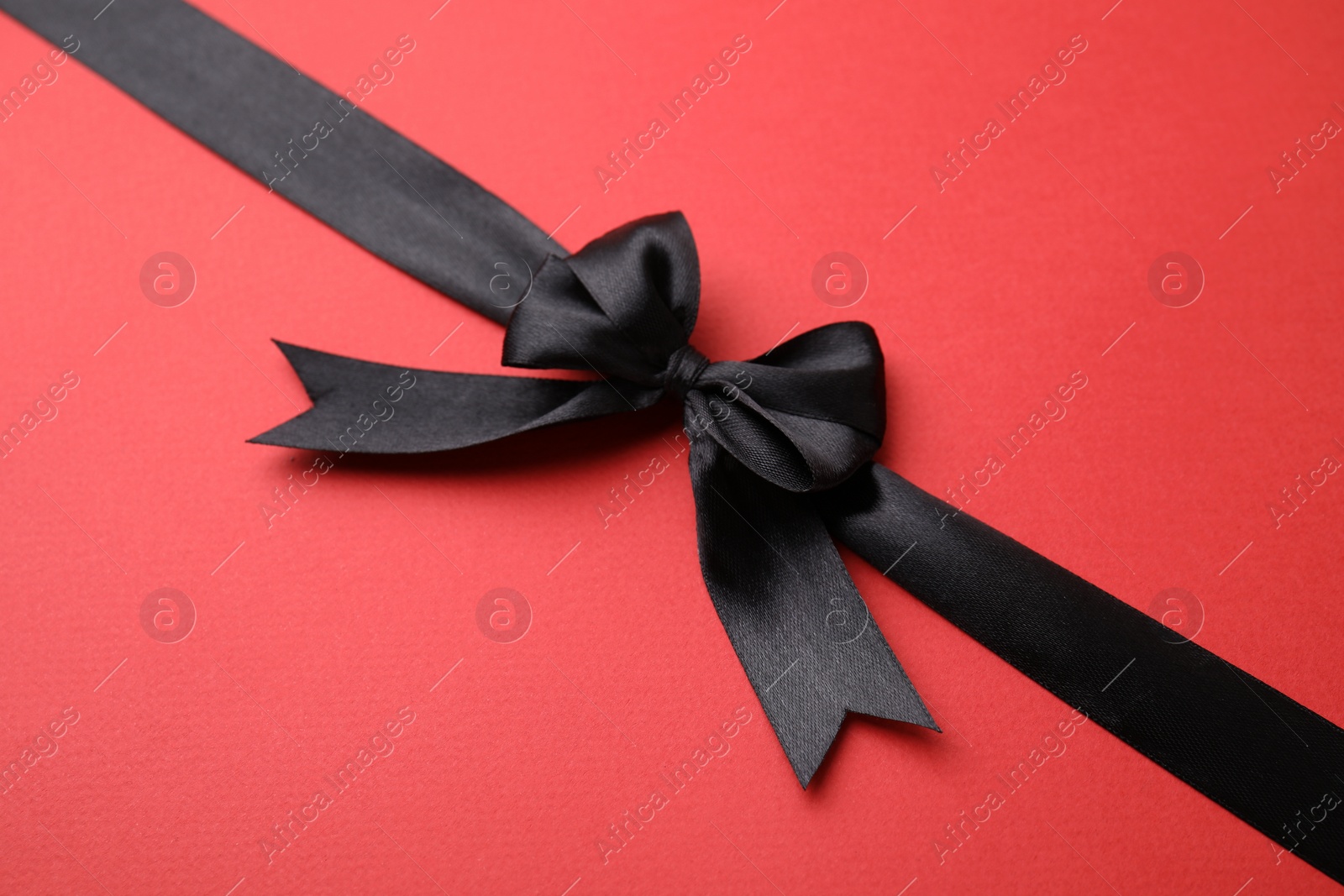 Photo of Black satin ribbon with bow on red background