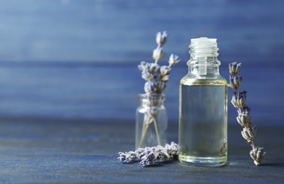 Bottle of natural essential oil and lavender flowers on blue wooden background. Space for text