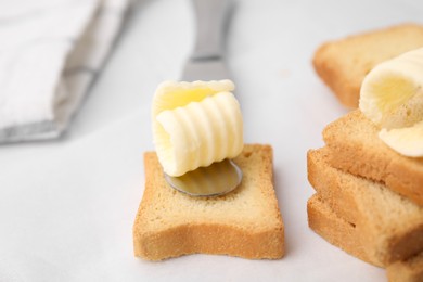 Photo of Tasty butter curls, knife and pieces of dry bread on white table, closeup