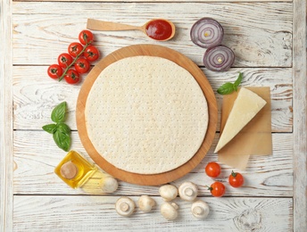 Flat lay composition with base and ingredients for pizza on wooden table