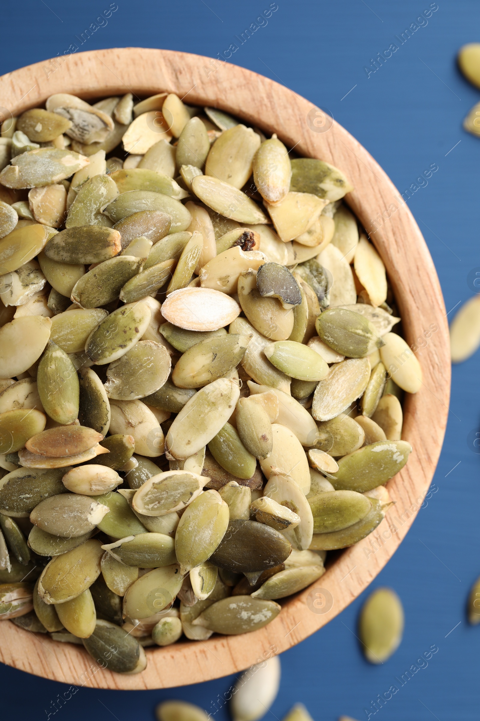 Photo of Bowl with peeled pumpkin seeds on blue wooden table, top view