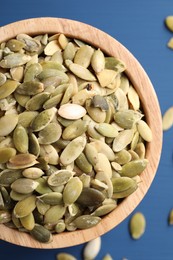Bowl with peeled pumpkin seeds on blue wooden table, top view