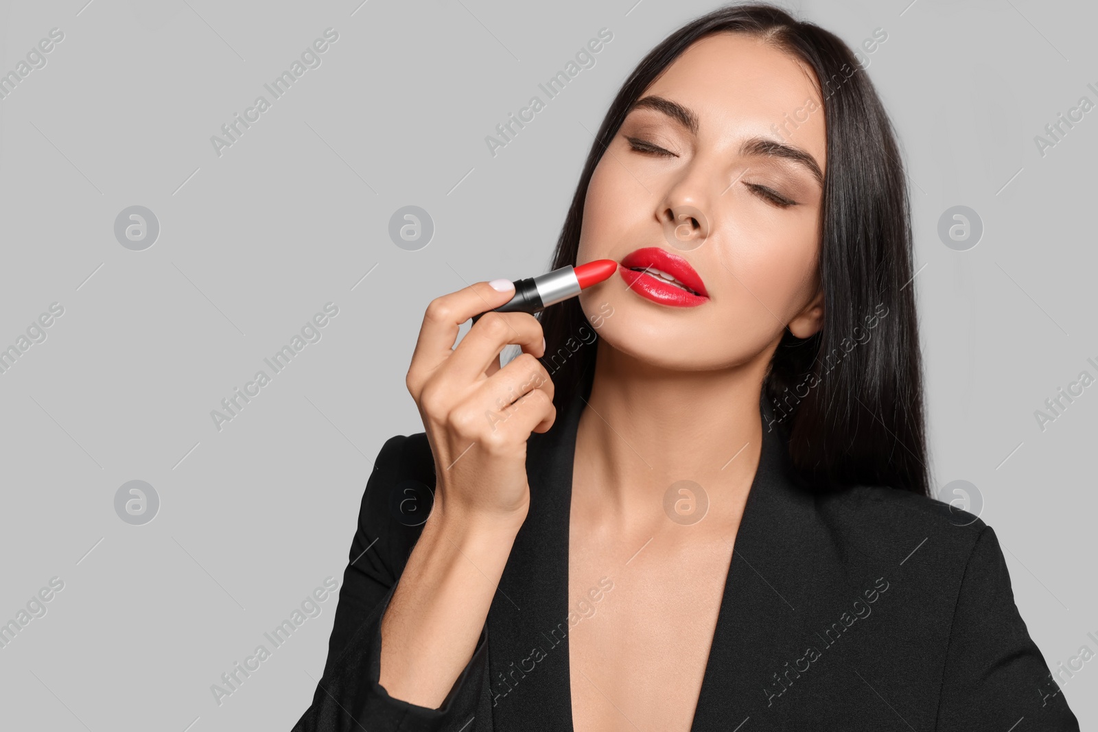 Photo of Young woman with beautiful makeup holding red lipstick on light gray background. Space for text
