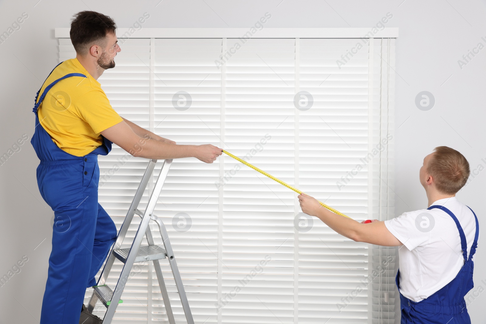 Photo of Workers using measuring tape while installing horizontal window blinds indoors