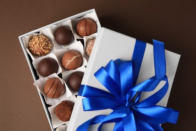 Photo of Box with delicious chocolate candies on brown background, top view