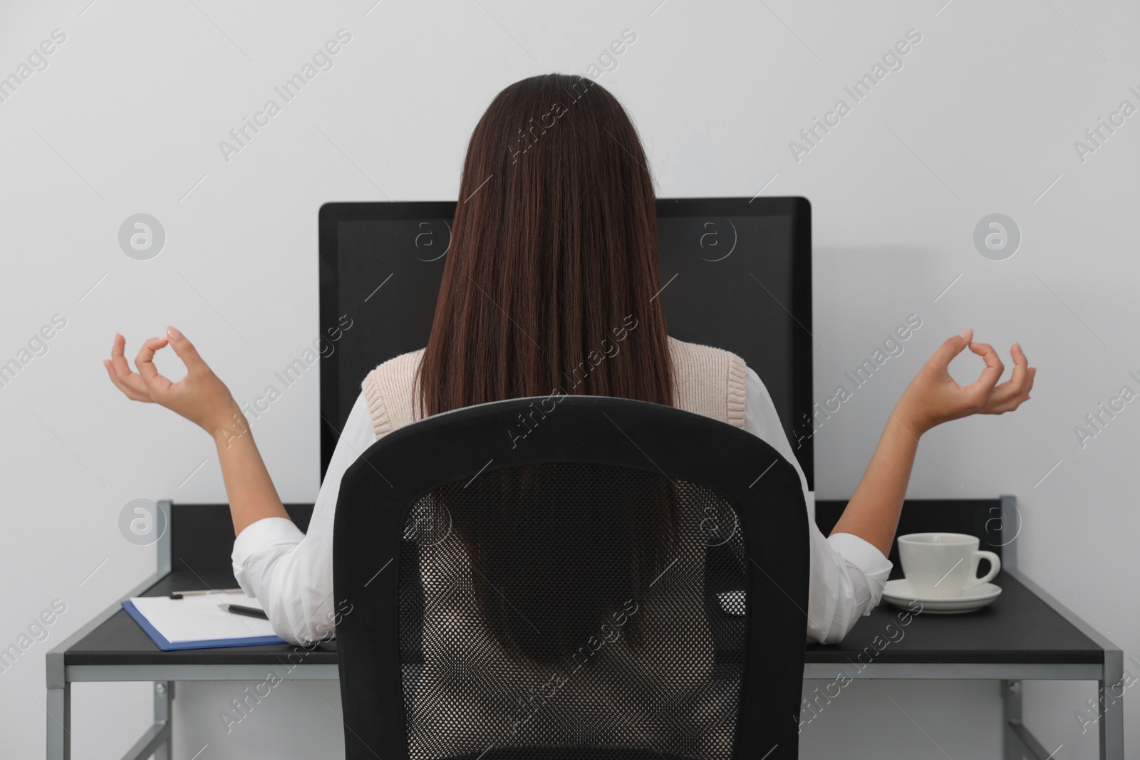 Photo of Businesswoman meditating at workplace, back view. Zen concept