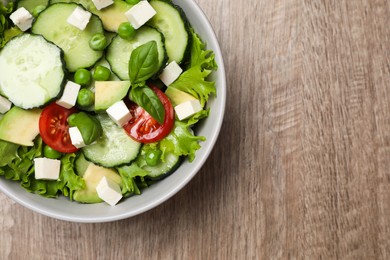 Photo of Tasty fresh salad with cucumber in bowl on wooden table, top view. Space for text