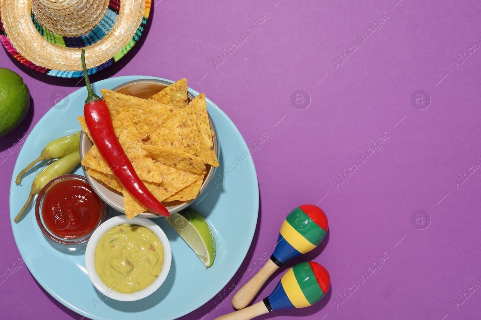 Photo of Nachos chips, guacamole, chili pepper, maracas and Mexican sombrero hat on purple background, flat lay. Space for text