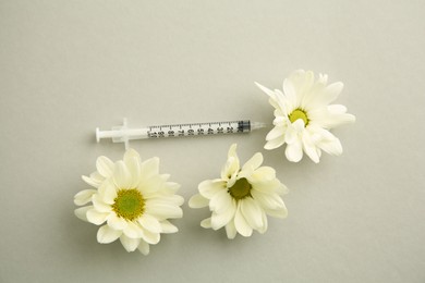 Photo of Medical syringe and beautiful chrysanthemum flowers on grey background, flat lay