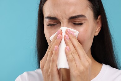 Photo of Suffering from allergy. Young woman blowing her nose in tissue on light blue background, closeup