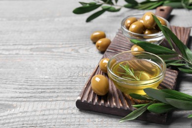 Photo of Bowl of cooking oil, olives and green leaves on wooden table. Space for text