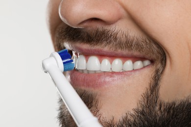 Photo of Man brushing his teeth with electric toothbrush on white background, closeup