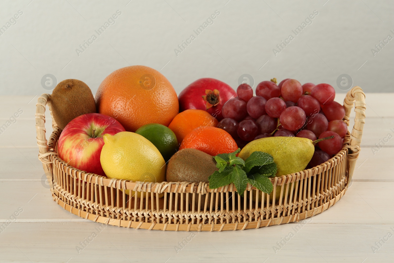 Photo of Fresh ripe fruits in wicker tray on white wooden table