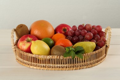 Fresh ripe fruits in wicker tray on white wooden table