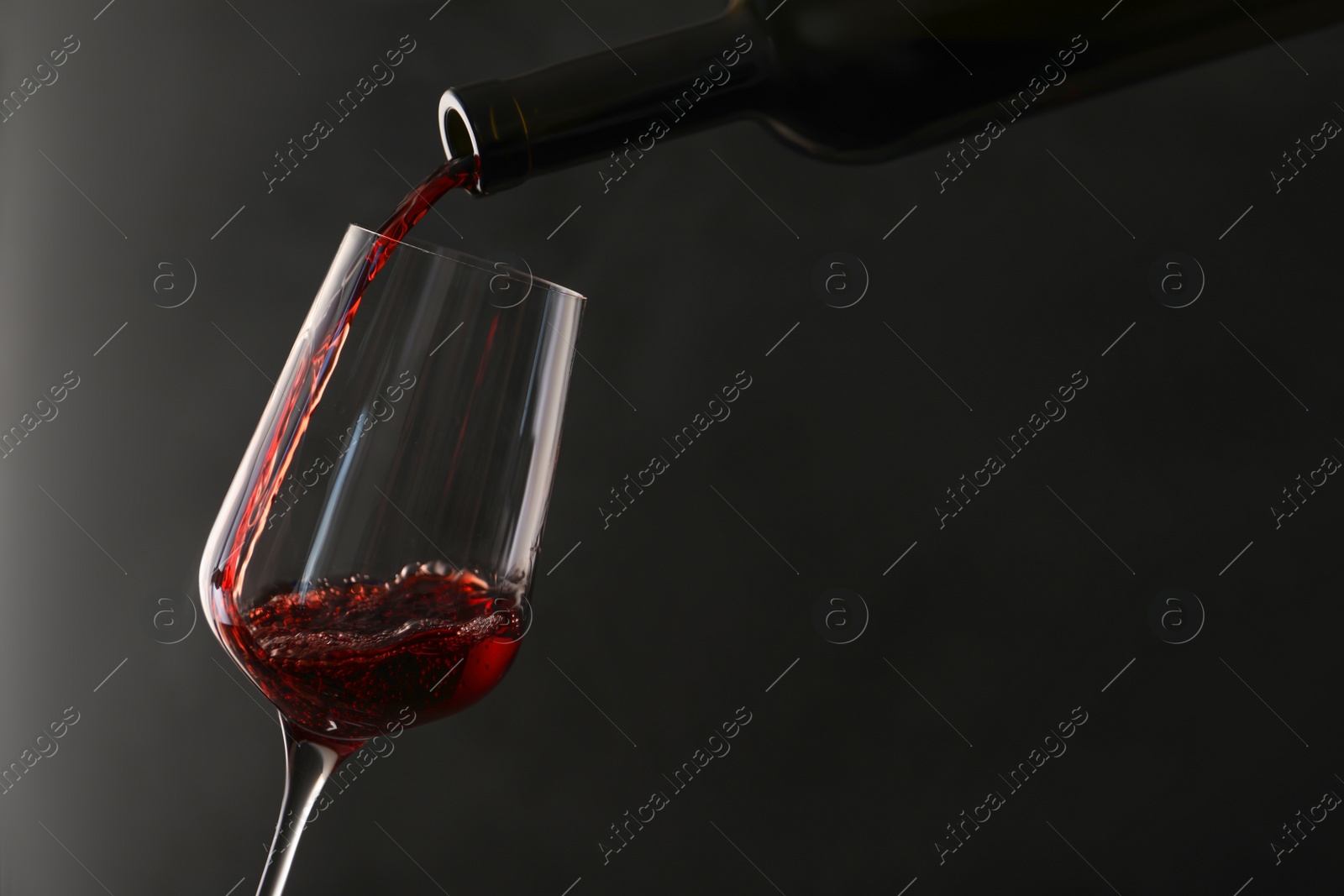 Photo of Pouring red wine from bottle into glass on dark background. Space for text