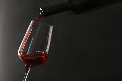 Pouring red wine from bottle into glass on dark background. Space for text